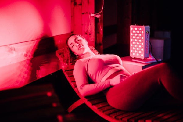 Vrouw ligt met gesloten ogen op een houten ligstoel naast een brandend paneel voor lichttherapie