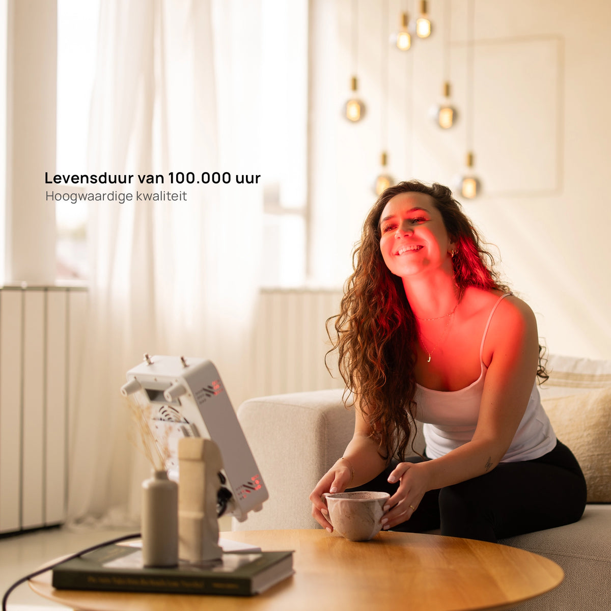 Vrouw op de bank behandelt haar gezicht en schouder met de Liroma Compact Gen5 roodlichtlamp op de salontafel